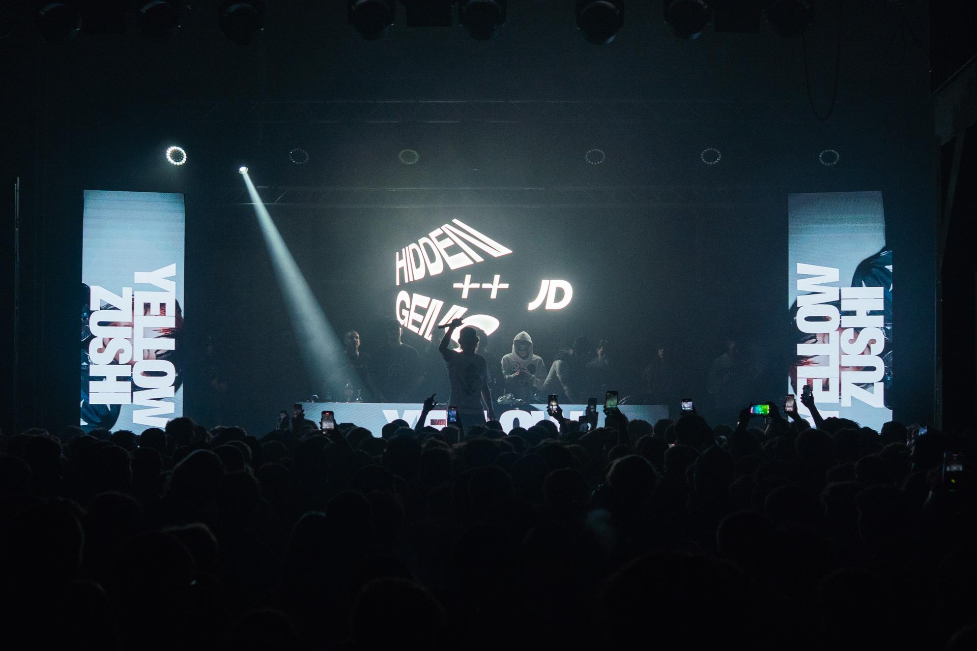 A wide audience perspective of the Hidden Gems stage, featuring large LED screens with event branding and performers silhouetted by bright stage lights.