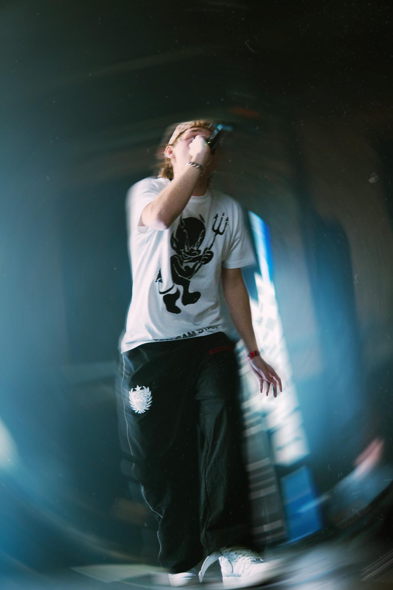 A dynamic photo of a vocalist wearing a graphic t-shirt and cap singing passionately into a microphone, framed by a strong motion blur effect.