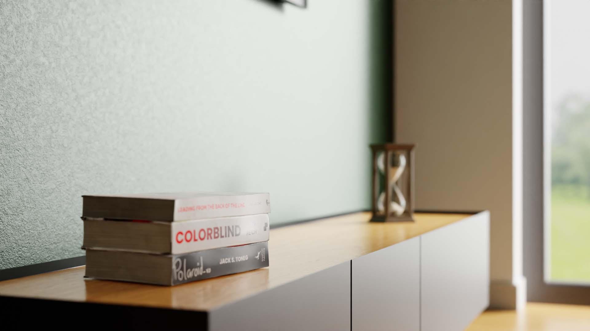 A detailed close-up shot of a minimalist wooden and dark grey media console. A stack of three books is on the surface: the top book title is 'COLORBLIND,' and the bottom book is titled 'Polaroid.' A wooden lantern sits in the background.