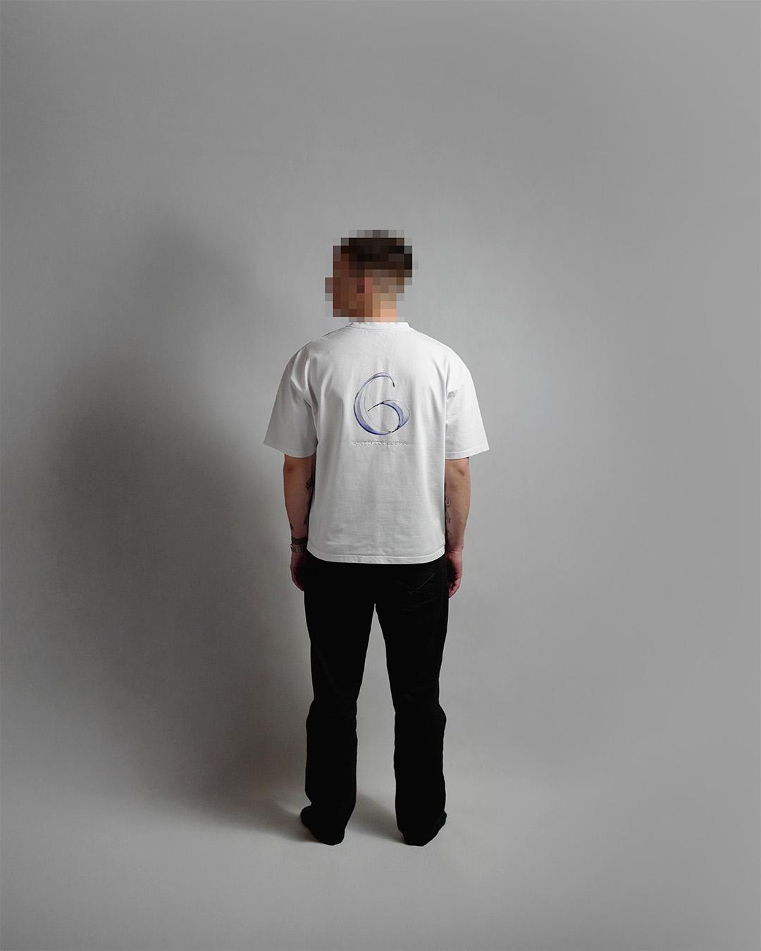 Back view of a model in a grey studio setting wearing a white t-shirt featuring a large metallic blue number 6 and 'sixth.collective' graphic